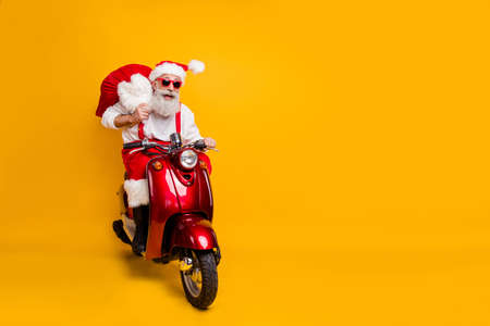 Full body photo of crazy funny santa claus in red hat drive hurry fast motor cycle hold sack christmas x-mas preparation ride north-pole wear shirt suspenders isolated yellow color backgroundの写真素材
