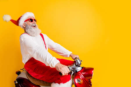 Profile photo of stylish santa white hair grandpa rushing x-mas theme party by retro bike wear trendy sun specs red trousers cap shirt isolated yellow color backgroundの写真素材