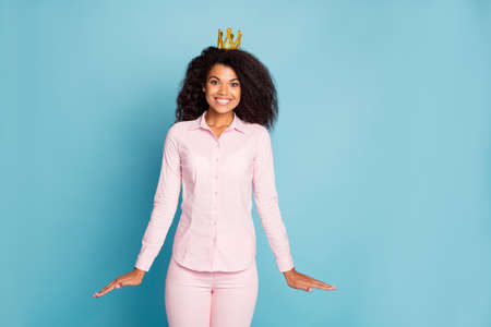 Photo of amazing dark skin wavy lady overjoyed to be prom queen shy person wear golden crown pink shirt pants isolated blue color backgroundの写真素材