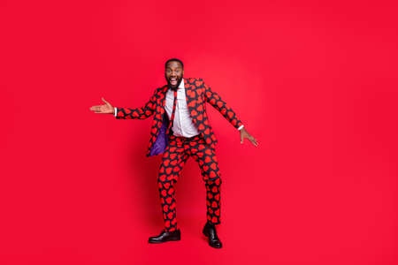 Full length photo of crazy dark skin man moving dancing playing amour cupid role at corporate valentine day party wear hearts pattern stylish suit isolated red color backgroundの写真素材