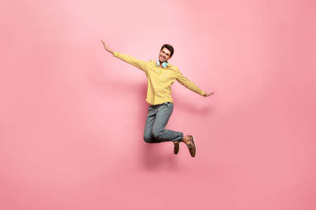 Full length photo of handsome guy jumping high enjoy summer time using earflaps flying like bird wear hipster striped shirt trousers isolated pink color backgroundの写真素材