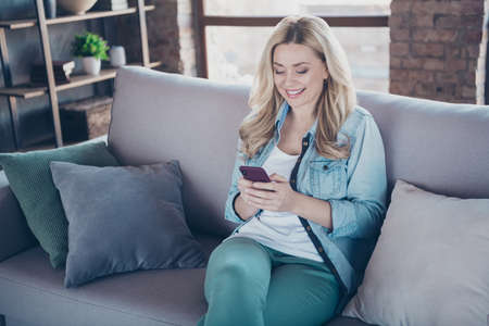 Portrait of her she nice attractive lovely pretty charming cheerful cheery wavy-haired lady sitting on divan using digital device gadget at modern industrial loft brick style interior living-roomの写真素材