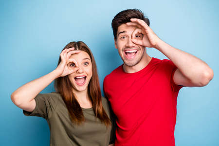 Portrait of funny cheerful funky two married people show okay sign make binocular watch neighbors amazed excited wear casual style clothing isolated over blue color backgroundの写真素材