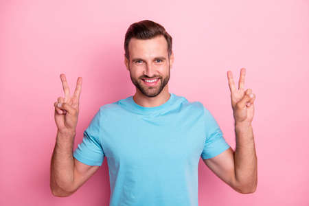 Photo of cheerful handsome man smiling, toothily showing you double v-sign isolated pastel color...