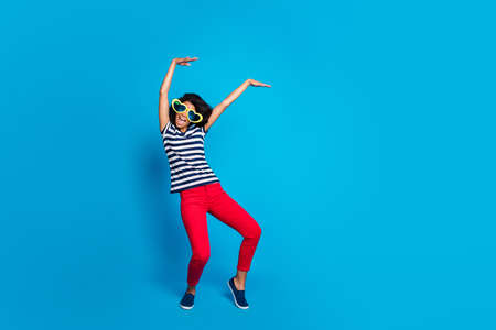 Lets party hard. Full body photo of funky crazy wavy hair mulatto girl have rest relax raise hands dance in nightclub wear heart-figure spectacles good look clothes isolated bright color backgroundの写真素材