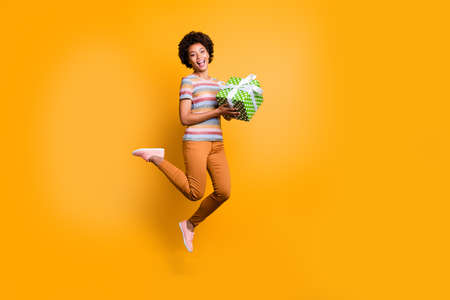 Full length body size turned photo of jumping girl holding giftbox with hands wearing pants trousers...