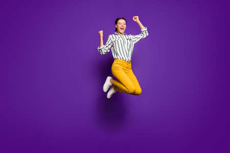 Full size photo of crazy pretty lady jumping high competitive sportswoman celebrating victory raising fists wear striped shirt yellow trousers isolated purple color backgroundの写真素材