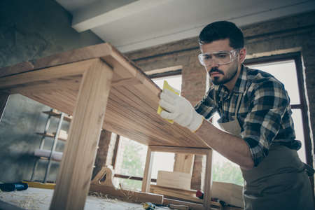 Low angle view photo of concentrated man hardwood worker renew wooden furniture slab table polish smooth surface in home house garageの写真素材