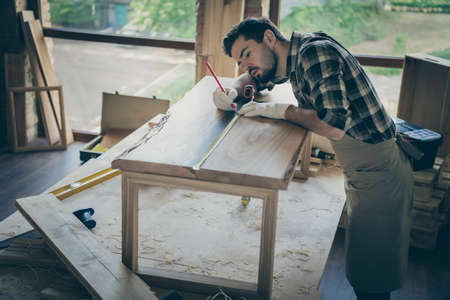 Concentrated workman man restore wooden slab table use pencil ruler measure length on desk surface in home house garageの写真素材