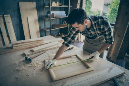 Photo of focused serious man concentrated on measuring length of wooden frame correctly by using...