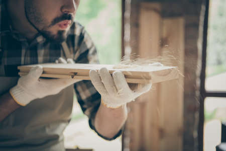 Cropped close up photo of serious confident man blowing sawdust away from wooden block before...