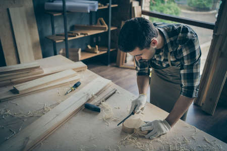 Photo of concentrated man processing wooden heart with chisel polishing in gloves working with...