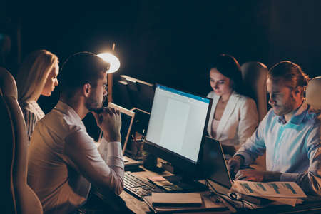 Portrait of nice attractive focused concentrated coworkers gathering preparing report researching financial data analyzing at night preparing report at work place station dark room indoorsの写真素材