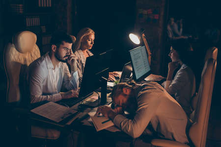 Nice attractive focused concentrated tired coworkers partners leaders gathering appointment preparing urgent report at night preparing report at work place station dark roomの写真素材