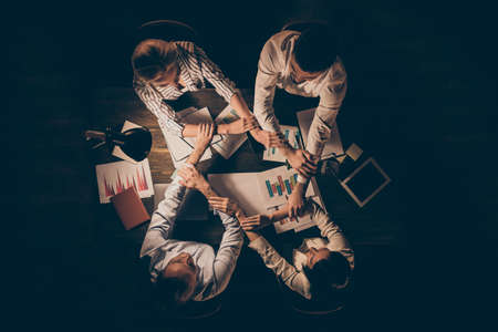 Top above high angle view of four hardworking people executive managers partners leaders shaking hands gathering over table desk at late night workplace workstationの写真素材
