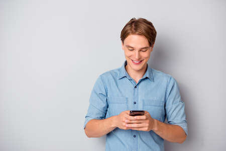 Portrait of positive cheerful guy use smartphone read social media news enjoy, wear stylish clothing isolated over grey color backgroundの写真素材