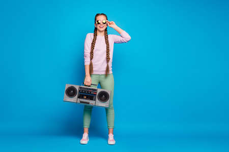 Full body photo of modern youth with braids pigtails girl hold retro boombox, feel crazy want party on spring holidays wear pink sweater sneakers green pants trousers isolated blue color backgroundの写真素材