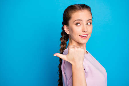 Closeup photo of pretty lady long braids indicating thumb finger empty space, low sale shopping prices wear casual pink pullover isolated blue color backgroundの写真素材