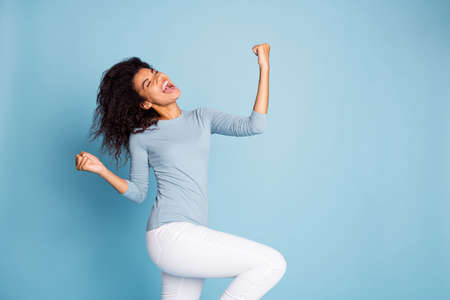 Turned photo of cheerful crazy excited overjoyed carefree girl screaming, making fists in white...