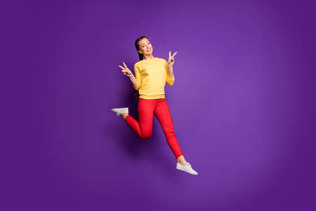 Full length photo of pretty teen lady jumping high having fun showing v-sign symbols wear casual...