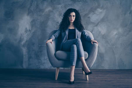 Portrait of her she nice-looking attractive pretty classy chic content serious authoritative wavy-haired girl sitting in chair crossed legs gray concrete wall backgroundの写真素材