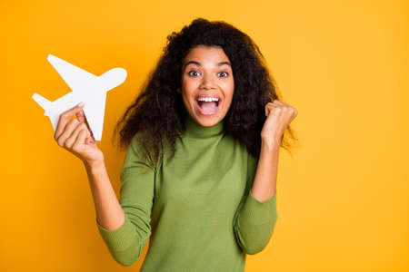 Photo of mixed-race positive cute pretty beautiful girl won tickets to go abroad by air plane rejoicing excited emotions holding plane isolated curly wavy yellow vivid color backgroundの写真素材