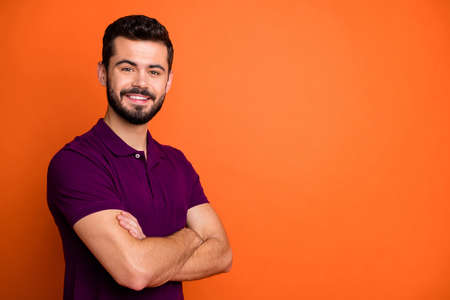 Photo of cheerful positive handsome man with arms crossed standing near empty space looking at you isolated orange vibrant color backgroundの写真素材