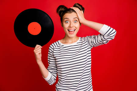 Retro discotheque concept. Amazed funny funky girl hold vinyl plate impressed scream wow omg wear striped white sweater isolated red color backgroundの写真素材