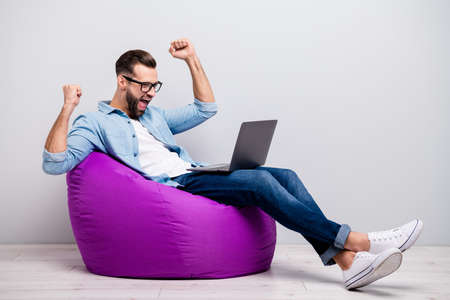 Full size profile photo of funny guy holding notebook sitting comfy, soft violet armchair celebrating startup success wear specs casual denim outfit isolated grey color backgroundの写真素材