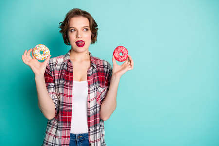 Portrait of lovely minded girl hold two donuts think yummy flavor lick lips addicted sweet lover...