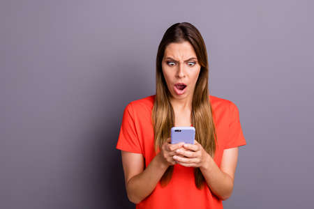 Omg unbelievable. Impressed frustrated girl use her smartphone read social network news got notification scream wear beautiful clothes isolated over grey color backgroundの写真素材