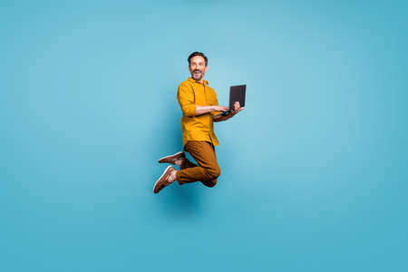 Full size photo of funky man feel rejoice emotions jump use laptop search social media online black friday discounts wear casual style clothing isolated over blue color backgroundの写真素材