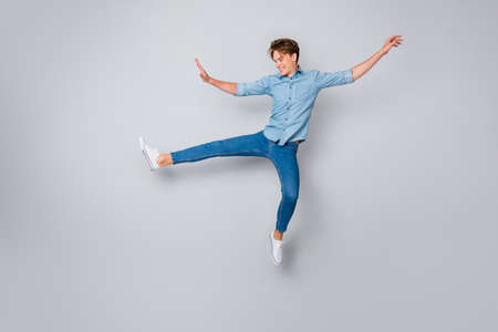 Full length photo of cheerful candid man jump raise hands legs imagine he child teen again wear...