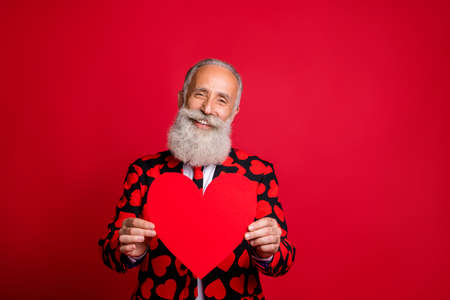 Portrait of his he nice attractive cheerful cheery kind friendly amorous, gray-haired guy holding in hand paper heart congrats isolated on bright vivid shine vibrant red color backgroundの写真素材