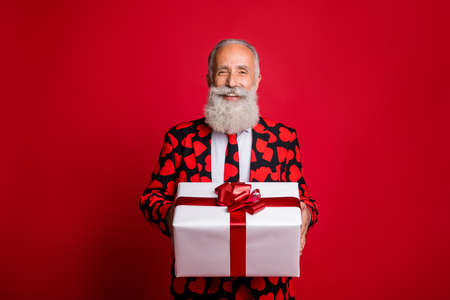 Photo of funky mature guy amour cupid character role showing big gift box holiday courier wear stylish hearts pattern suit costume shirt tie isolated red color backgroundの写真素材