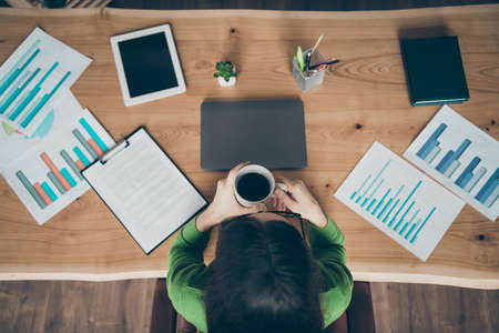 High angle above view photo of pretty business lady holding hot drink, mug look paper sheets company money income sit chair wear green turtleneck office room indoorsの写真素材