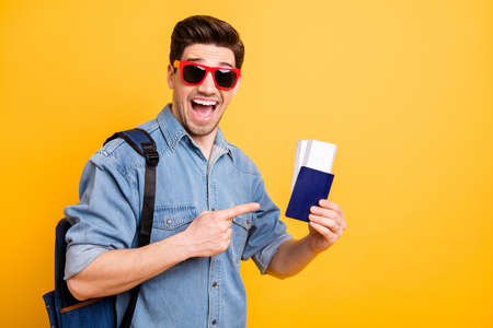 Portrait of his he nice attractive funky cheerful cheery glad guy demonstrating passport id tour trip tickets isolated over bright vivid shine vibrant yellow color backgroundの写真素材