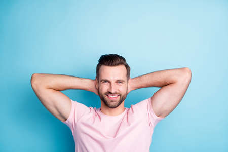 Photo of attractive guy holding hands behind head enjoy amazing weekend day relaxing refreshment moment wear casual pink t-shirt isolated blue color backgroundの写真素材