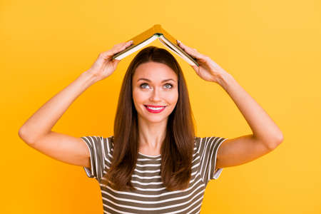 Close up photo of cheerful college student girl put her textbook above head enjoy after study free time break wear good looking clothes red pomade isolated yellow color backgroundの写真素材