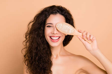Close-up portrait of her she nice attractive gorgeous winsome cheerful cheery feminine wavy-haired girl closing covering one eye new professional comb isolated over beige pastel backgroundの写真素材