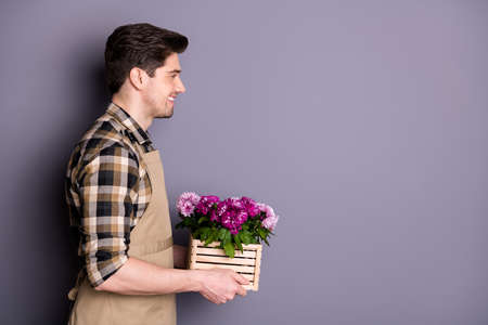 Profile photo of attractive worker guy hold hands pink flowers growing in pot advising buy fresh flowers avoid cutting down wear apron plaid shirt isolated grey color backgroundの写真素材