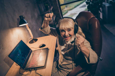 Portrait of her she nice attractive cheerful cheery satisfied gray-haired blonde grandma playing game contest battle championship win great success at industrial loft modern concrete style interiorの写真素材