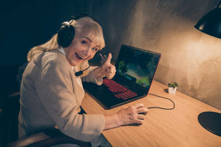 Portrait of her she nice cheerful cheery gray-haired blonde grandma playing game showing thumbup advice contest battle championship win at industrial loft modern concrete style interiorの写真素材