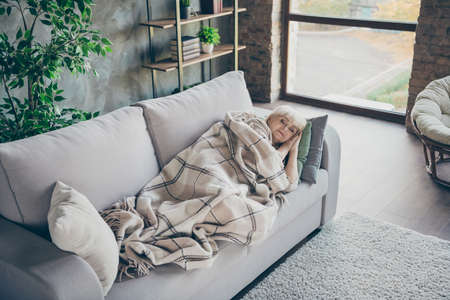 Photo of amazing blond aged granny having daydream lying comfort sofa divan covered plaid blanket dreamy cute hold hands under head living room indoorsの写真素材