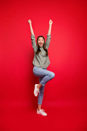 Full size vertical photo of funny lady yelling loud raising fists celebrating sports game match victory rejoicing wear casual grey green shirt jeans isolated red color backgroundの写真素材