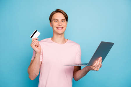 Photo of attractive guy holding notebook plastic wireless card making online purchase advising new easy shopping way wear casual pink t-shirt isolated blue color backgroundの写真素材