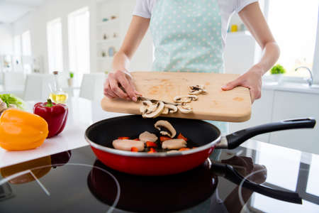 Cropped photo of housewife hands holding cutting wooden board checking, meat condition adding fresh mushrooms cooking tasty dinner white light kitchen indoorsの写真素材