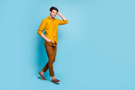 Turned photo of handsome guy holding hand in pants pocket holding his hair wearing yellow shirt...