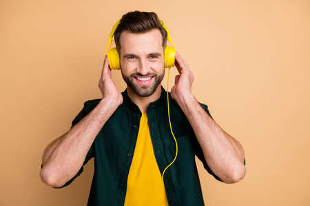 Photo of nice handsome hipster guy holding hands cool modern yellow earphones listening popular songs good mood wear casual outfit isolated beige color backgroundの写真素材