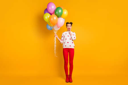 Full size photo of funny lady hold colorful air balloons open mouth unexpected surprise wear hearts pattern sweater red pants shoes isolated yellow color backgroundの写真素材